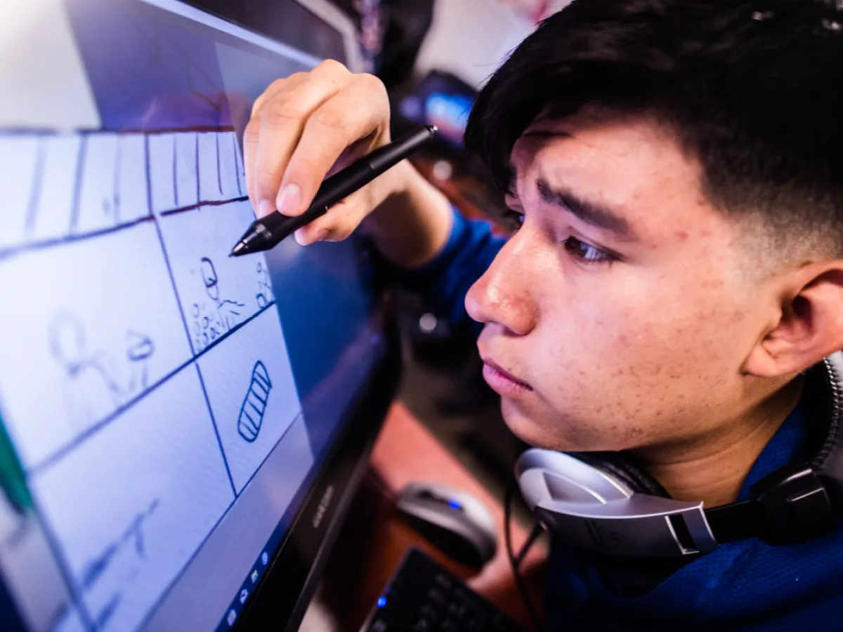 A student uses a stylus to draw storyboard sketches on a large digital screen