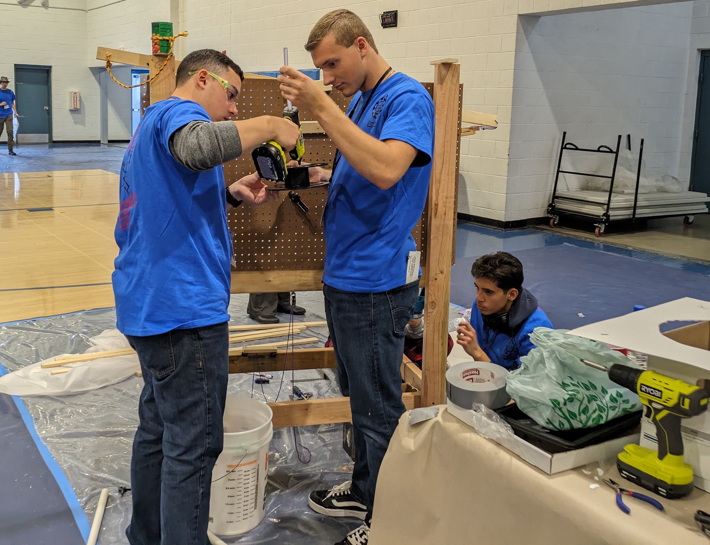 Two students in clue shirts working with tools on a wood construction project