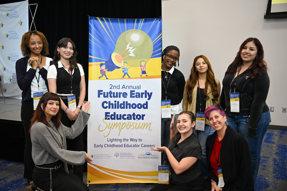 Future educators standing next to a banner for a symposium