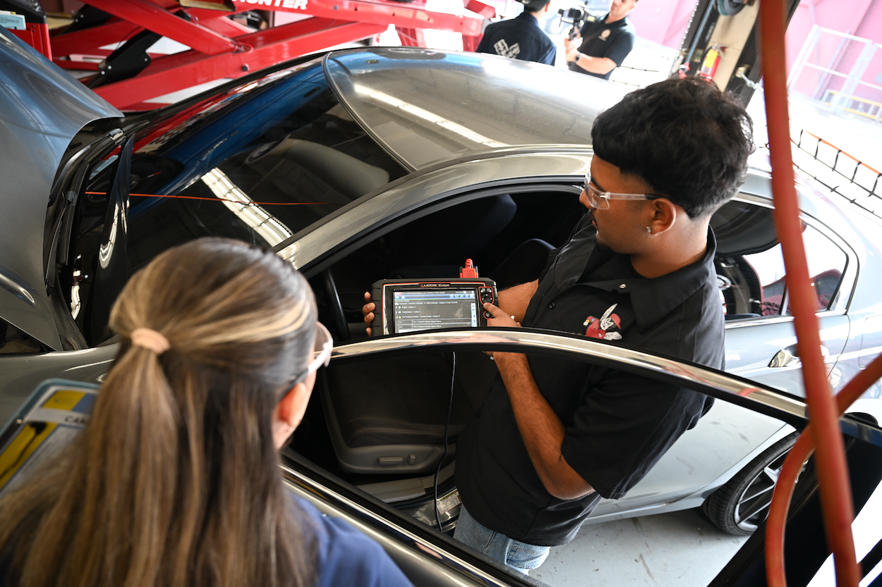 Automotive students using a computer device to check for car issues and showing another student the readings